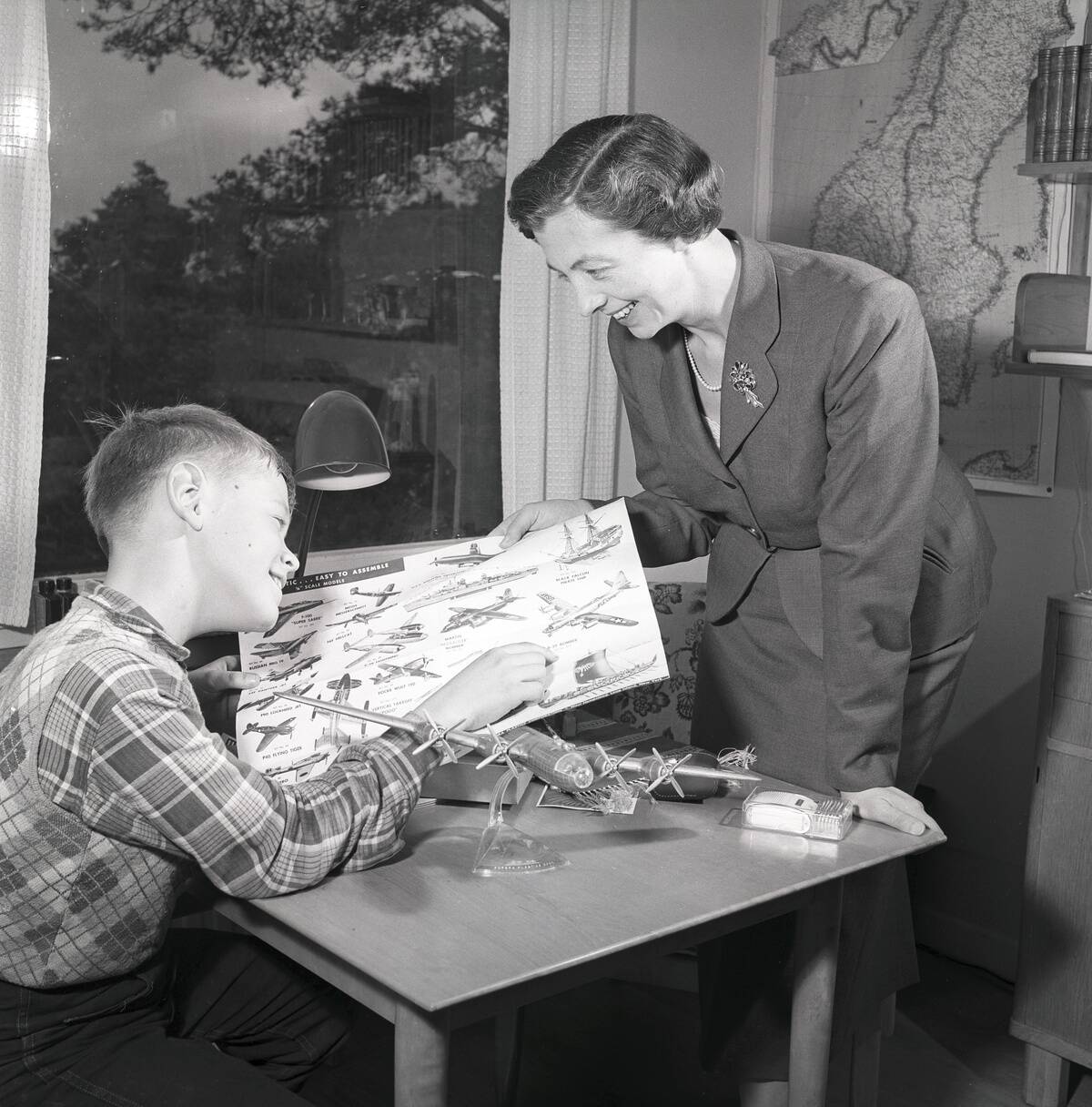Hobby in the 1950s. A boy is sitting at a table with a plastic model of an American bomb aircraft B29...